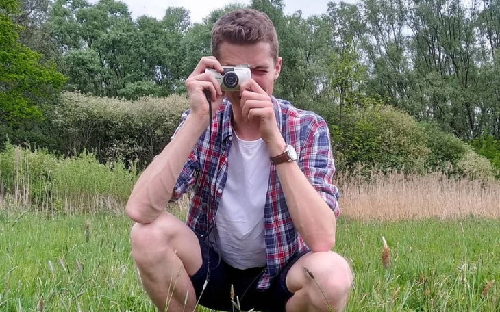 Mężczyzna fotografujący w plenerze, siedzący na trawie.
