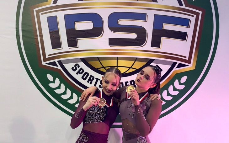 Dwie dziewczyny z medalami, pozujące na tle logo IPSF.