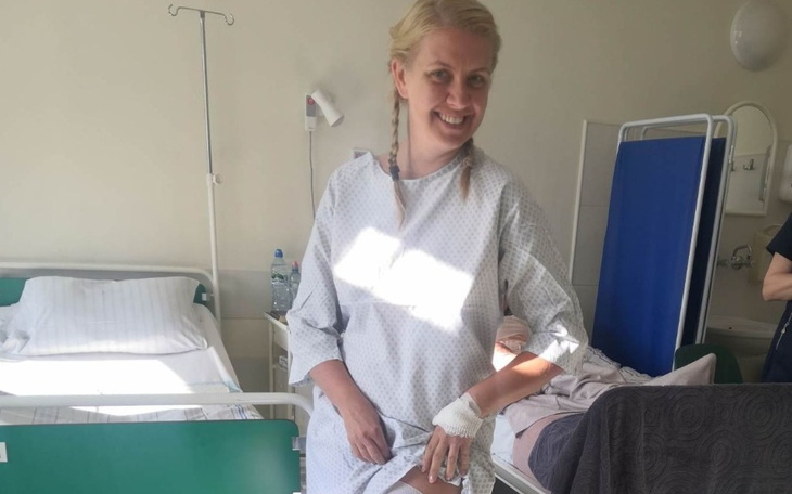 Kobieta w szpitalu, uśmiechnięta w szpitalnej koszuli.