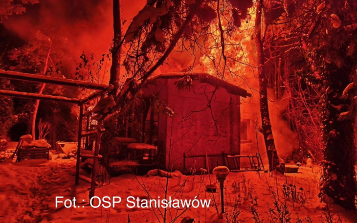 Płonący budynek w lesie, otoczony dymem.