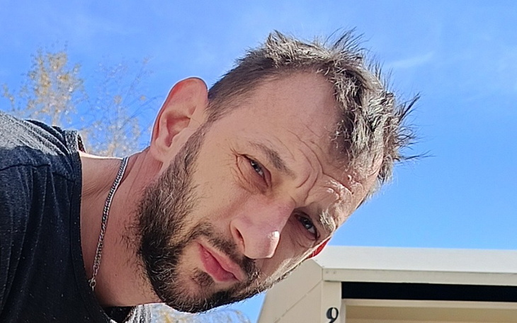 Mężczyzna z krótkimi włosami, patrzący w kamerę, w tle niebo.