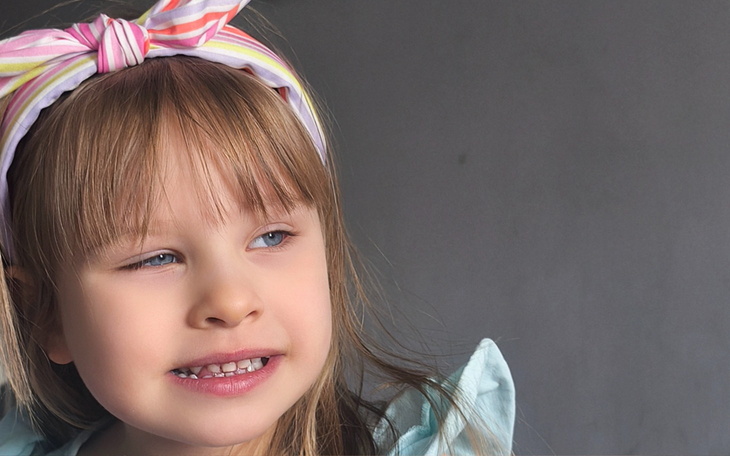 Mała dziewczynka z opaską na głowie, uśmiechająca się.