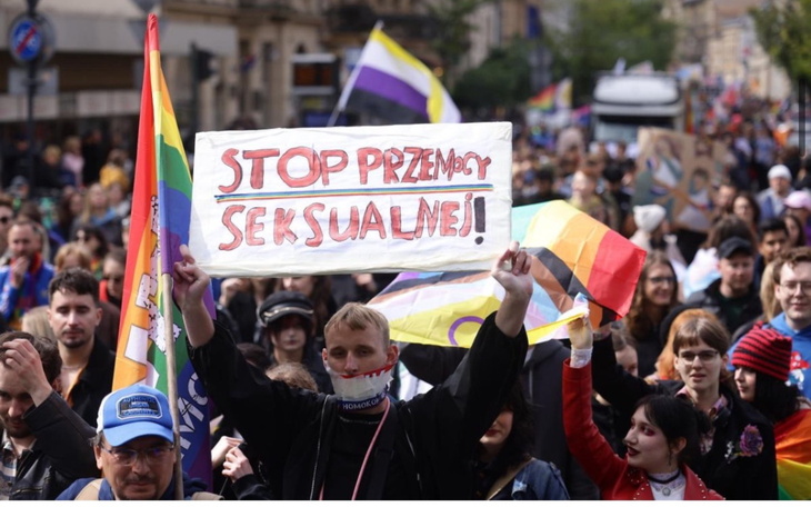 Tłum ludzi na demonstracji z transparentem przeciw przemocy seksualnej.