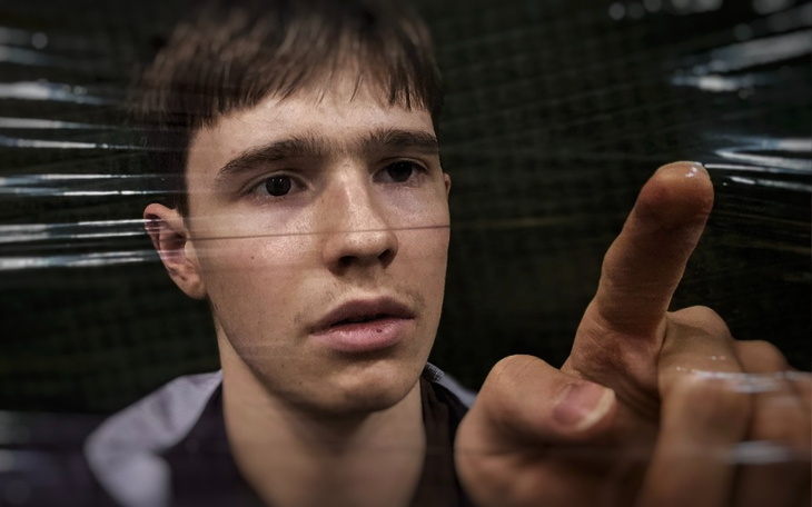 Młody mężczyzna dotykający przezroczystą folię, z zamyśloną miną.