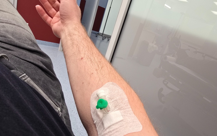 Ujęcie ręki w opatrunku z zieloną blocką na ramieniu w szpitalnym wnętrzu.