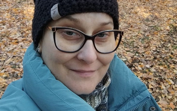 Kobieta w okularach, uśmiechająca się na tle jesiennych liści.