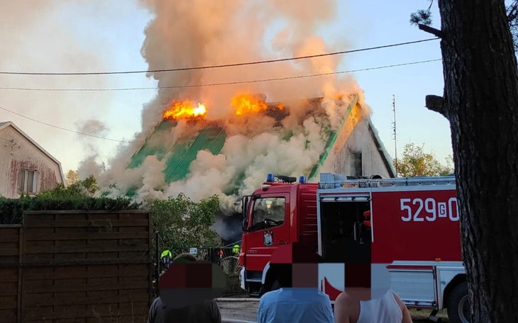 Pożar dachu budynku, z wozem strażackim w tle.