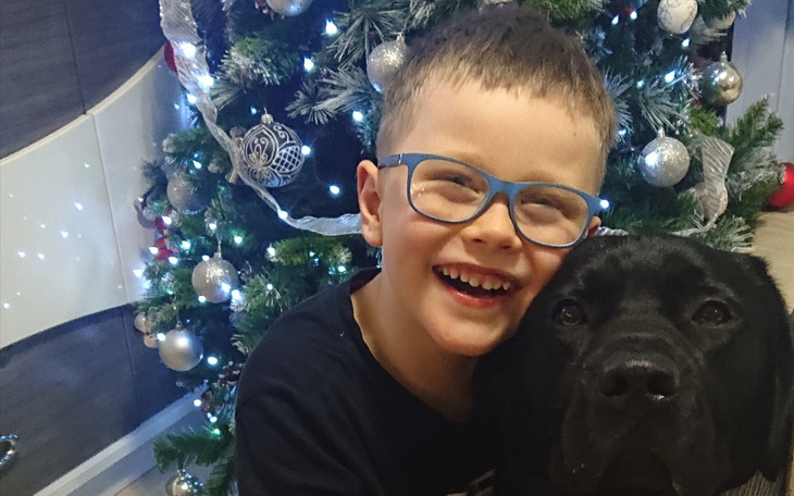 Chłopiec przytulający czarnego psa przy choince.