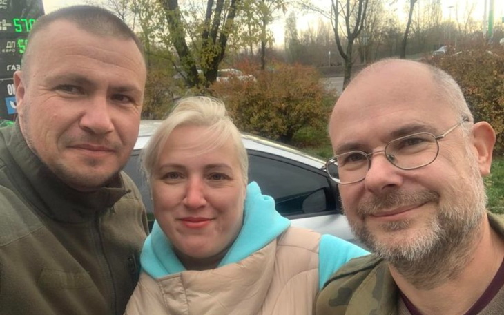 Trzy osoby pozujące do zdjęcia na tle samochodu.