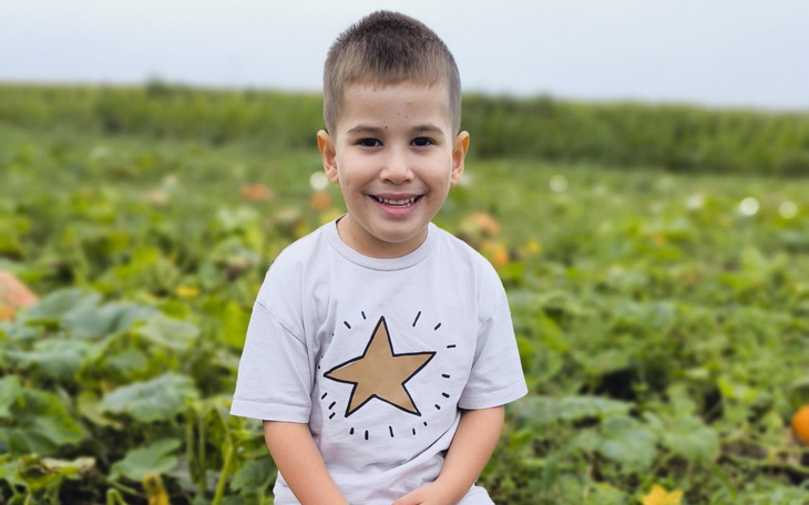 Uśmiechnięty chłopiec w koszulce z gwiazdą, na tle pól.