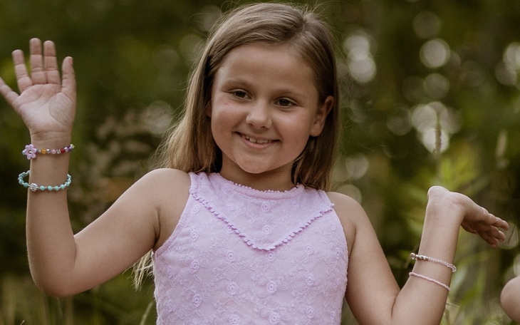 Uśmiechnięta dziewczynka w różowej sukience, machająca ręką.