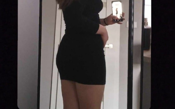 Kobieta w czarnej sukience, robiąca selfie w lustrze.