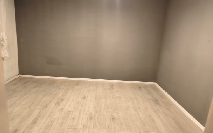 Pusty pokój z szarymi ścianami i drewnianą podłogą.