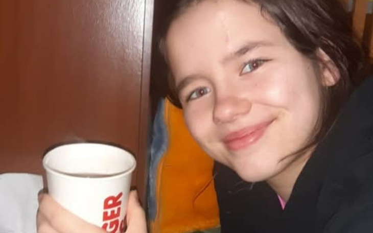 Młoda dziewczyna uśmiechająca się z kubkiem w ręku.