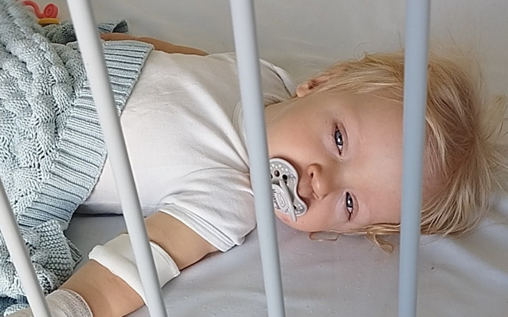 Małe dziecko w łóżku szpitalnym z smoczkiem.