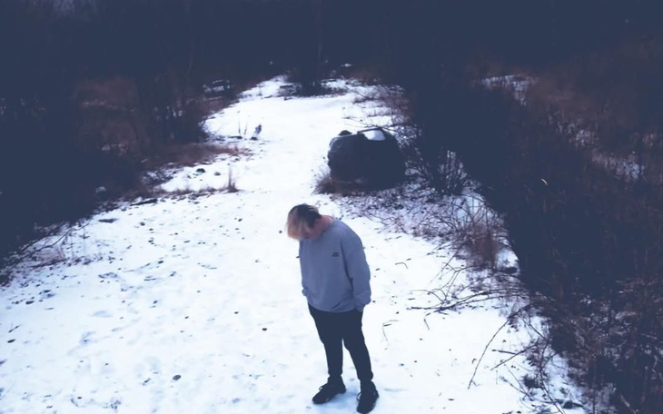 Osoba stojąca na śniegu, z głową pochyloną w dół, otoczona przez przyrodę.