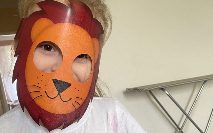Dziecko w masce lwa, uśmiechnięte i radosne.