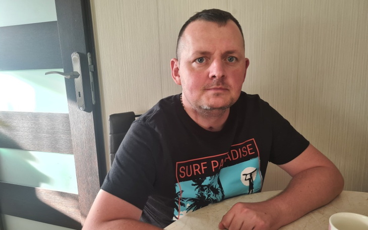 Mężczyzna siedzący przy stole, z poważnym wyrazem twarzy.