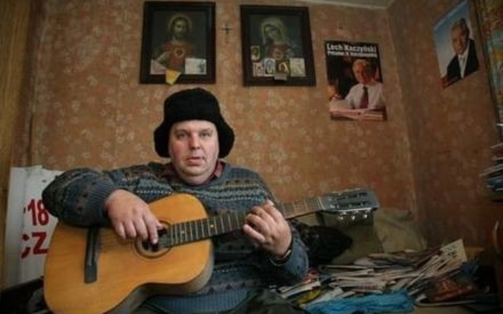 Mężczyzna grający na gitarze w skromnym wnętrzu.