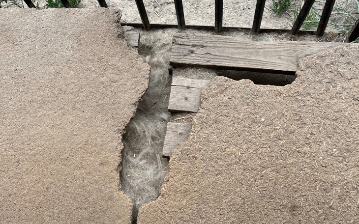 Uszkodzona nawierzchnia z widocznymi szczelinami i drewnianymi elementami.