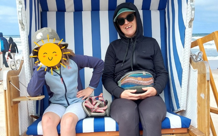 Dzieci na plaży, jedna z nich z uśmiechem zasłonięta słońcem.