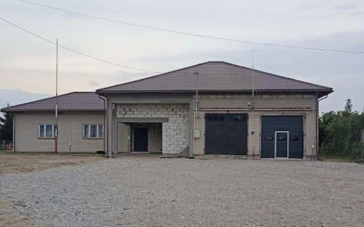 Widok na budynek z szarym dachem, otoczony terenem.