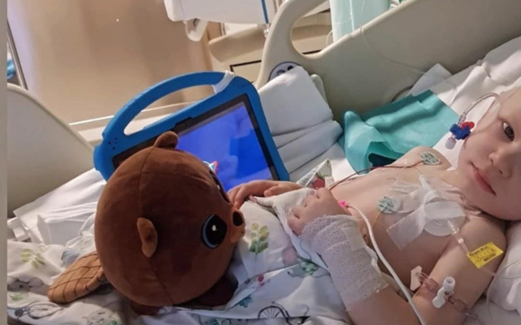 Chłopiec w szpitalu z pluszowym misiem i tabletem, wygląda na zrelaksowanego.