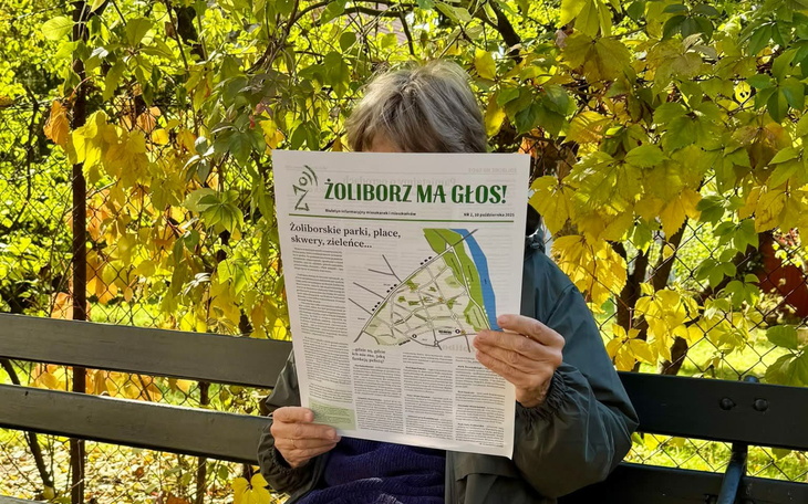 Osoba czytająca gazetę w parku wśród zieleni.