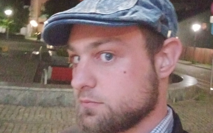 Mężczyzna w czapce, patrzący w stronę kamery, z wyrazem twarzy zamyślonym.