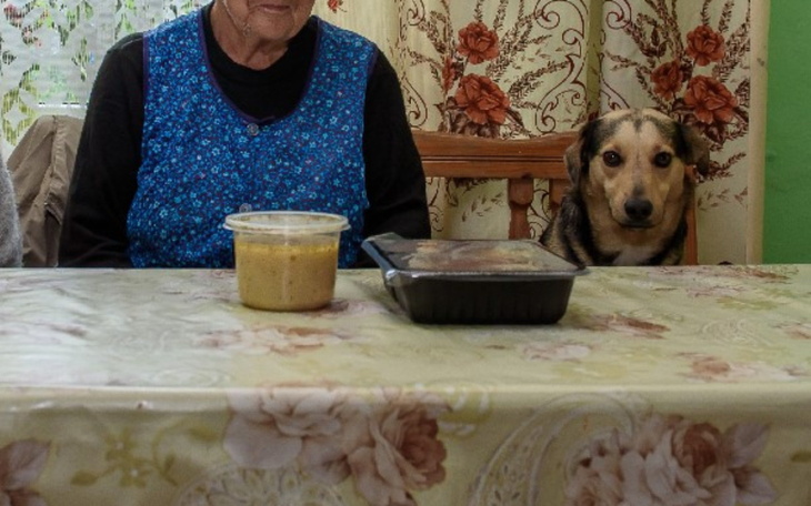 Starsza kobieta siedząca przy stole z psem obok.