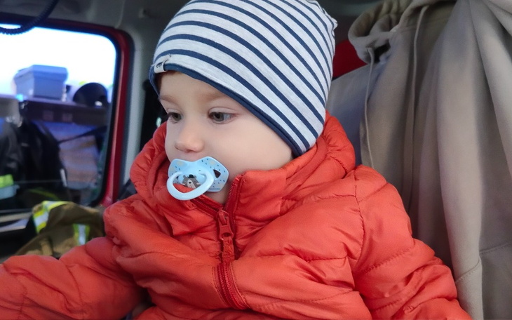 Mały chłopiec w pomarańczowej kurtce i czapce w paski.