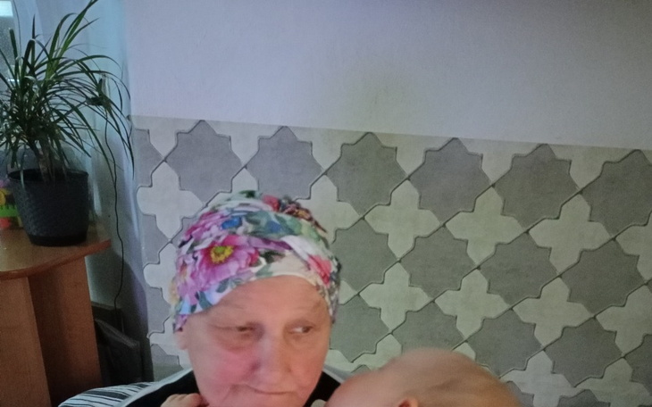 Starsza kobieta trzymająca niemowlę, z uśmiechem na twarzy.
