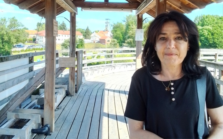 Kobieta na drewnianym tarasie z widokiem na zielony krajobraz.