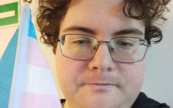 Osoba z okularami, trzymająca flagę w kolorach tęczy.