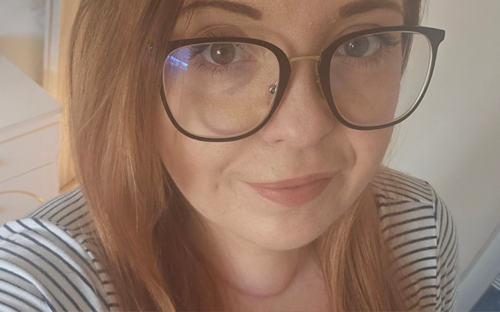 Portret kobiety w okularach, uśmiechającej się do kamery.