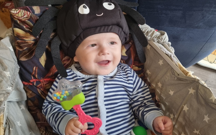 Uśmiechnięte dziecko w zabawnym kapeluszu pająka, bawiące się kolorowymi zabawkami.