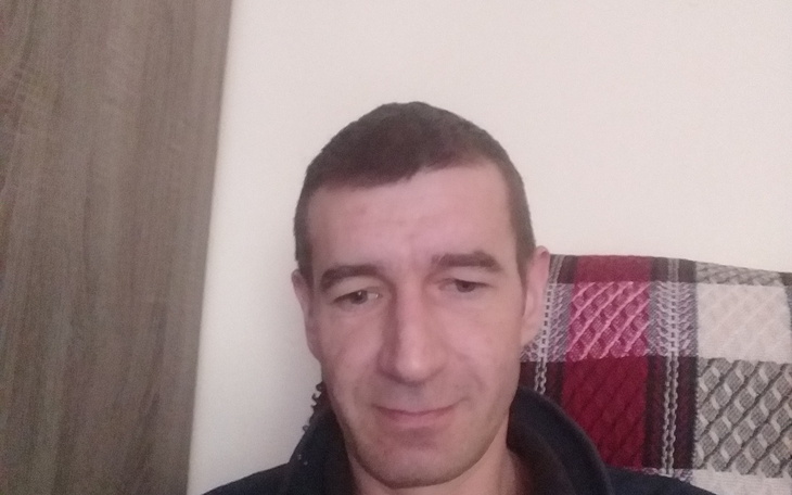 Mężczyzna siedzący na kanapie, uśmiechający się do kamery.
