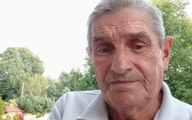 Starszy mężczyzna z poważnym wyrazem twarzy, w naturalnym otoczeniu.