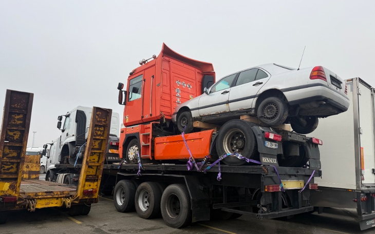 Złomowisko z ciężarówką i samochodem osobowym na przyczepie.