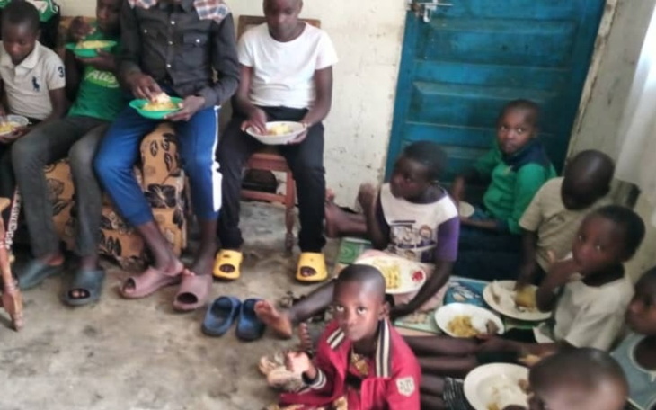 Grupa dzieci jedzących posiłek w skromnym pomieszczeniu.