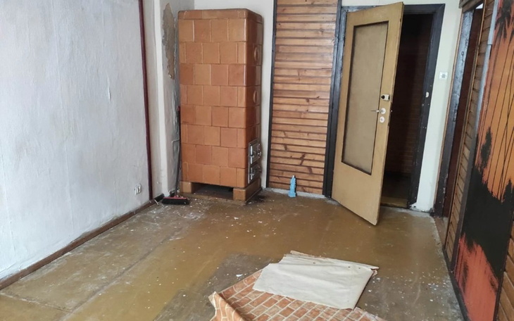 Pusty pokój z widoczną piecem i otwartymi drzwiami.