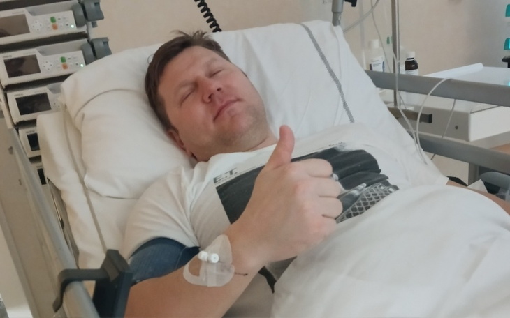 Mężczyzna w szpitalu, uśmiechający się i pokazujący kciuk w górę.