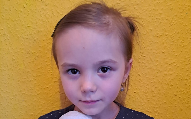 Mała dziewczynka z uśmiechem, trzymająca pluszowego misia, na żółtym tle.