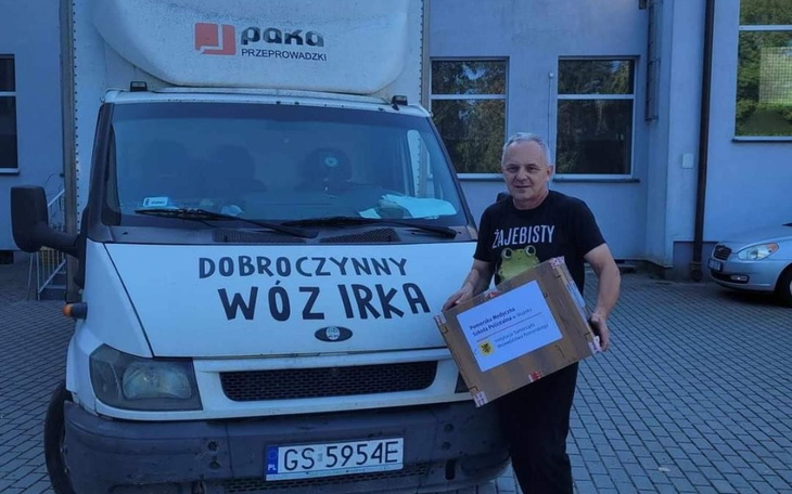 Mężczyzna trzymający paczkę przed samochodem z napisem 'Dobroczynny Wóz Irka'.