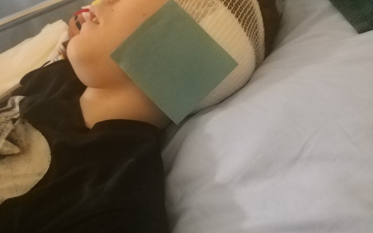 Chłopiec leży w łóżku z opatrunkiem na głowie.