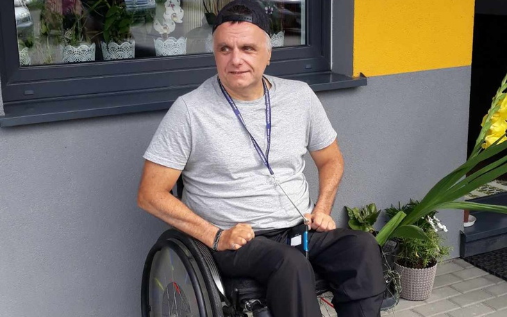 Mężczyzna na wózku inwalidzkim, uśmiechający się do kamery.