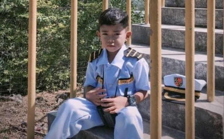 Chłopiec w mundurze, siedzący na schodach, wygląda na dumny.