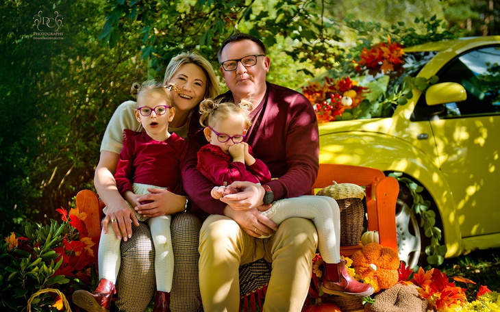 Rodzina pozująca na tle kolorowych liści i samochodu.