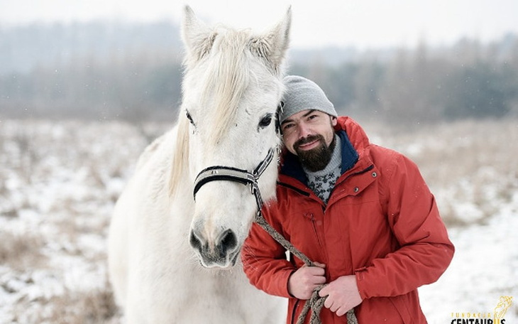 Mężczyzna z białym koniem na tle zimowego krajobrazu.