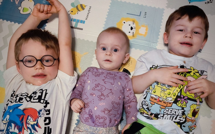 Troje dzieci leżących na podłodze, uśmiechniętych i radosnych.